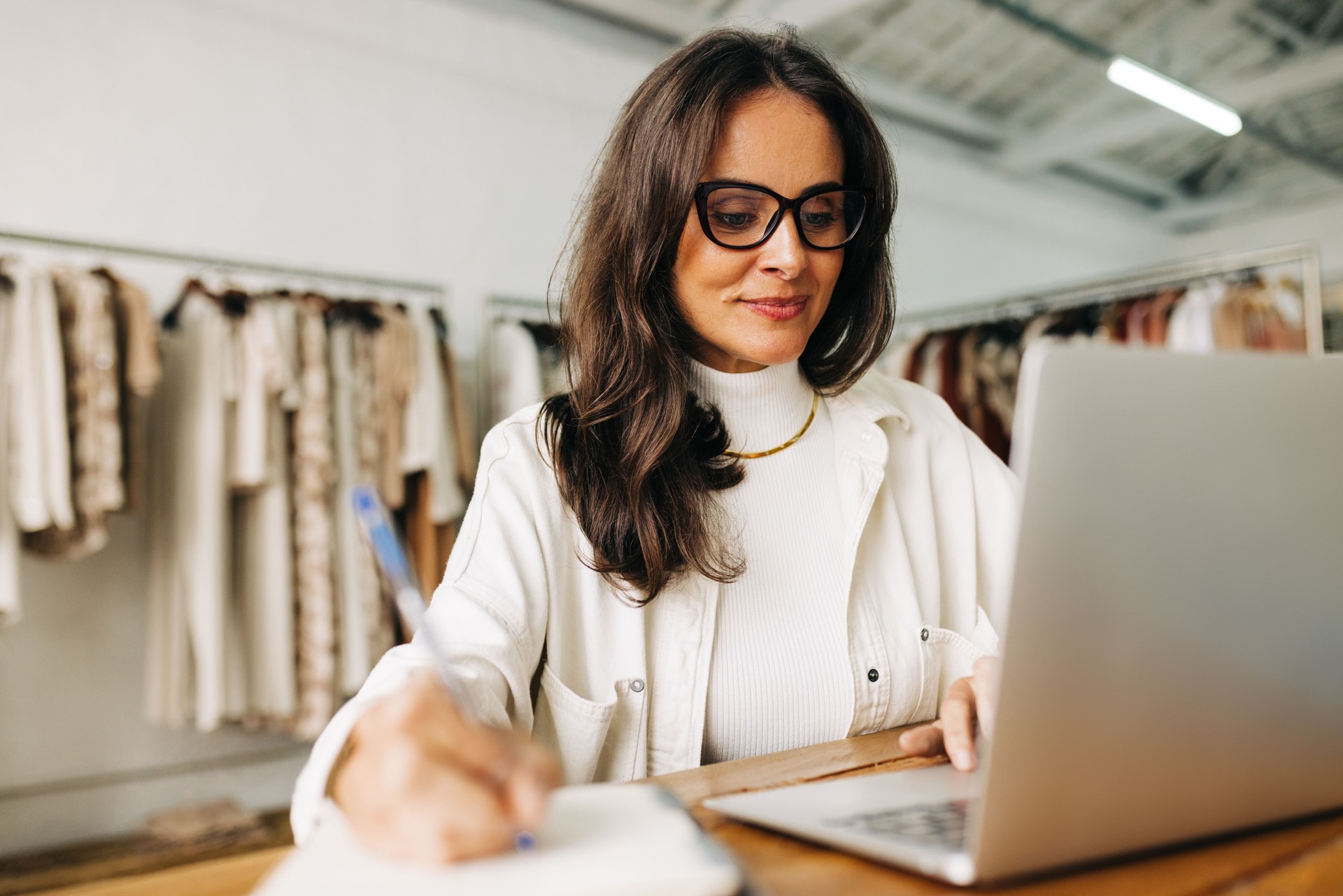 Small business plans: Woman using a laptop as she brainstorms in her clothing shop